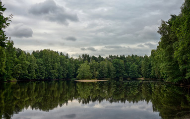 Fototapeta na wymiar Ruhiger, stiller Waldsee mit bewölktem Himmel und Spiegelung