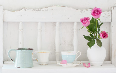 pinc roses in vase and dinnerware on white wooden shelf
