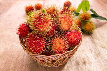 Fototapeta premium Fresh ripe red rambutans fruit in basket on wood floor. Rambutan is tropical of Southeast Asia fruit.