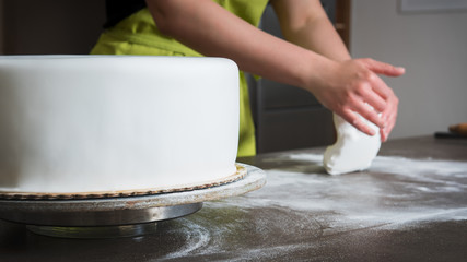 Unrecognisable woman preparing white fondant for cake decorating, hands detail, focus on the cake