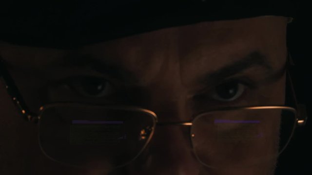 A hacker in a dark room reflected in the monitor