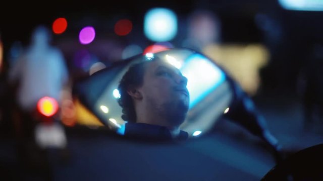 Young bearded handsome man drives the motorcycle in night reflected in mirror on blurred bokeh light night beautiful background. 1920x1080