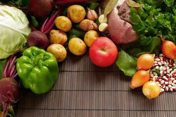 A set of fresh produce on a brown wooden background. A set of vegetables and meat for cooking red borsch