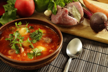 White plate with red borsch on the table near a set of fresh vegetables and meat