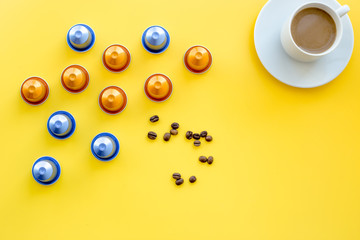 Beverage capsules for coffee mashine near coffee cup and grains on yellow background top view copyspace