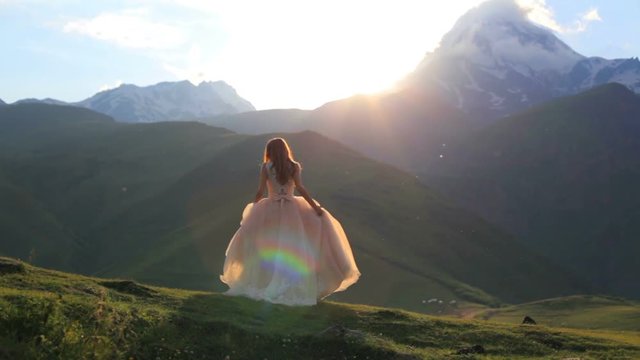 beautiful girl in a chic dress dances in the evening against the backdrop of the mountains and the setting sun