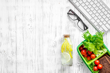 Light summer office lunch with cherry tomatoes, salad, bread near keyboard on wooden background top view copyspace