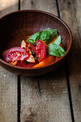 Slices of tomatoes and branches of basil - salad in a bowl on a wooden table