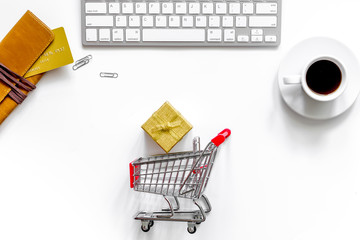 Buy gift in webstore. Gift box near shopping trolley, wallet and keyboard on white background top view copyspace