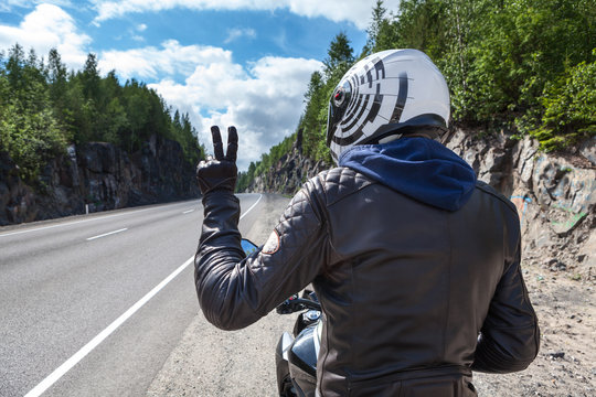 Motorcycle driver rear view at the asphalt road, sitting on motorbike and showing victory sign wit hand