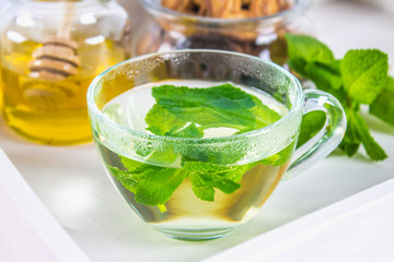 Mint tea in a cup, a jar of honey, a cookie in a jar, on a white tray in bed.