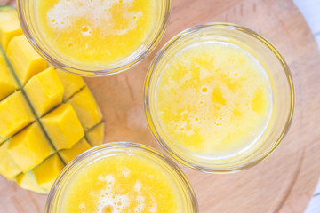 Yellow smoothie of mango, banana and orange on a white wooden table.