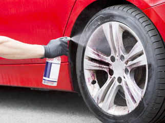 Caucasian man is spraying cleaner or washing liquid to alloy wheel. 