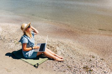 Young beautiful woman sitting with laptop on the beach near the sea