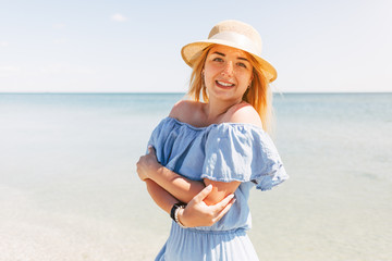 Young beautiful woman in blue dress walks along the beach at sea