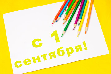 The inscription in Russian - From 1 September. On a sheet of white paper surrounded by colored pencils, markers, paints on a bright yellow background.