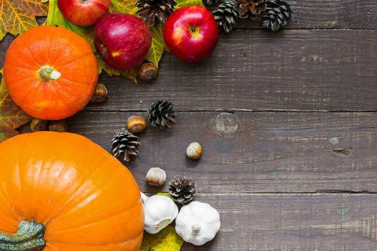 thanksgiving background with pumpkin, apples, acorns, garlic and fall leaves on the old wooden background