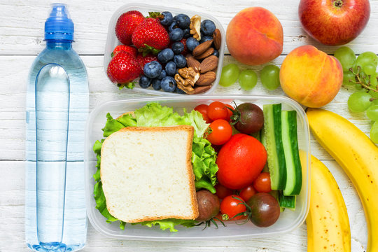 School lunch boxes with sandwich, fresh fruits and vegetables, berries and nuts and bottle of water