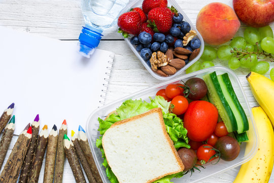 school lunch boxes with sandwich, fruits, vegetables and bottle of water with colored pencils