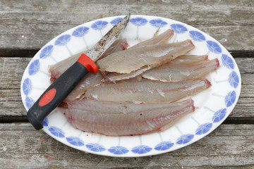 Gutted perch fish and a knife laying on a plate on a bridge