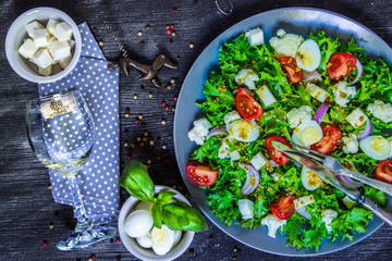Salad of fresh vegetables and a glass of wine on a black wooden background.