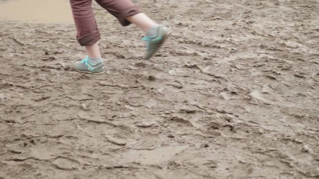 Guy in blue sport shoes walking on muddy ground.Slow motion