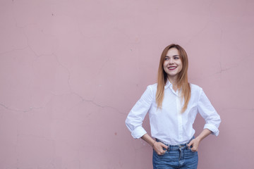 A woman stands at a bright wall in a white shirt and smiling