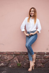 A girl stands in a pink wall wearing a white shirt and jeans