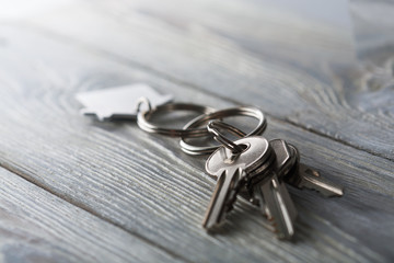 Keys to house with keychain on white wooden background