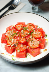 Strawberry and watermelon salad, served with crushed nuts and fresh basil served on a white plate.