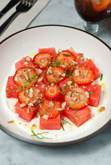 Strawberry and watermelon salad, served with crushed nuts and fresh basil served on a white plate.