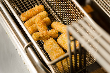 A silver deep pan industrial kitchen oil fryer, with golden oil, bubbling and frying potatoes