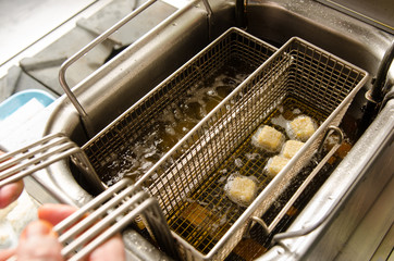 A silver deep pan industrial kitchen oil fryer, with golden oil, bubbling and frying potatoes