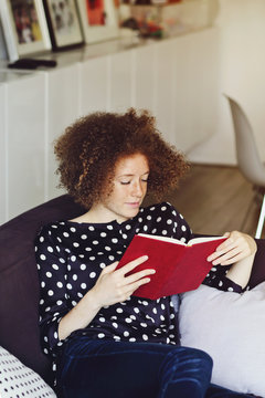 jeune femme rousse lisant un livre dans un intérieur maison