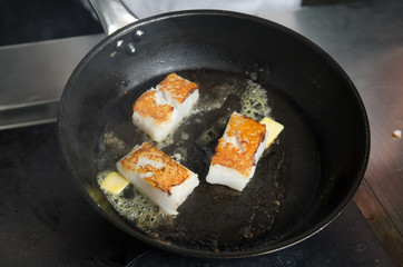 Pan fried golden fish fillet cubes, frying in real butter, in a non stick rustic pan.