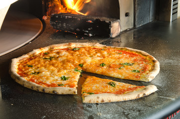 Gourmet Margherita pizza fresh from the pizza oven, with wood flame in the background