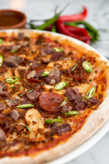 Spicy pepperoni, chicken and bacon pizza with jalapeño slices and chilli peppers in the background