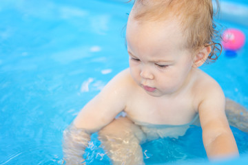 Sixteen months old baby girl playing in the plastic pool with her toys; baby covered with sun protection cream; happy and care free childhood concept