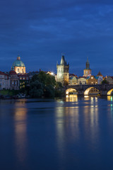 Fototapeta na wymiar Lit Charles Bridge (Karluv most) and old buildings at the Old Town and their reflections on the Vltava River in Prague, Czech Republic, at dusk.