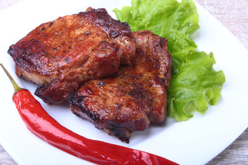 Steak of grilled meat and chili pepper with tomato, lettuce leaves on white plate.