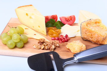 Assortment of cheese with fruits, grapes, nuts and cheese knife on a wooden serving tray.