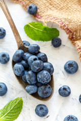 Spoon with blueberries on a white stone table.