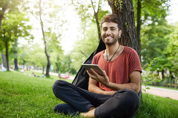 Stylish bearded man with appealing dark eyes smiling into camera having pleased expression sitting...