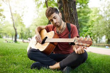 Handsome good-looking male playing musical instrument outdoors. Bearded guy with stylish haircut...