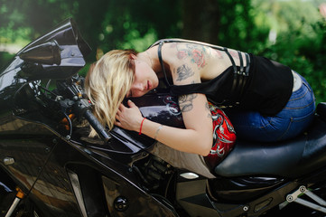 Obraz na płótnie Canvas The blond girl lies on a motorcycle, smiles eyes, sensual and cheerful, hair closes her eyes