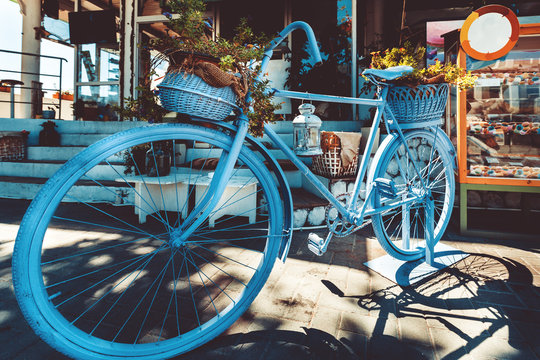 Retro Vintage Blue Bicycle With Basket Of Flowers On Cobblestone Street