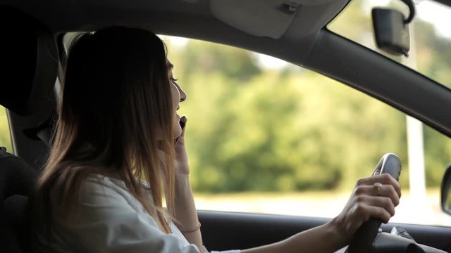 Cute girl talking on the phone behind the wheel of the car
