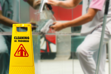 The warning signs cleaning in progress in the building and the maid working in the back