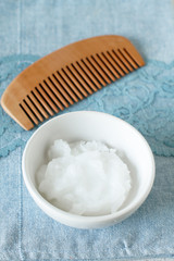 Organic coconut oil in a ceramic jar on blue background. Hair treatment.