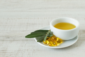 Close-up of bowl with olive oil, natural pills and olive branch kept on wooden table